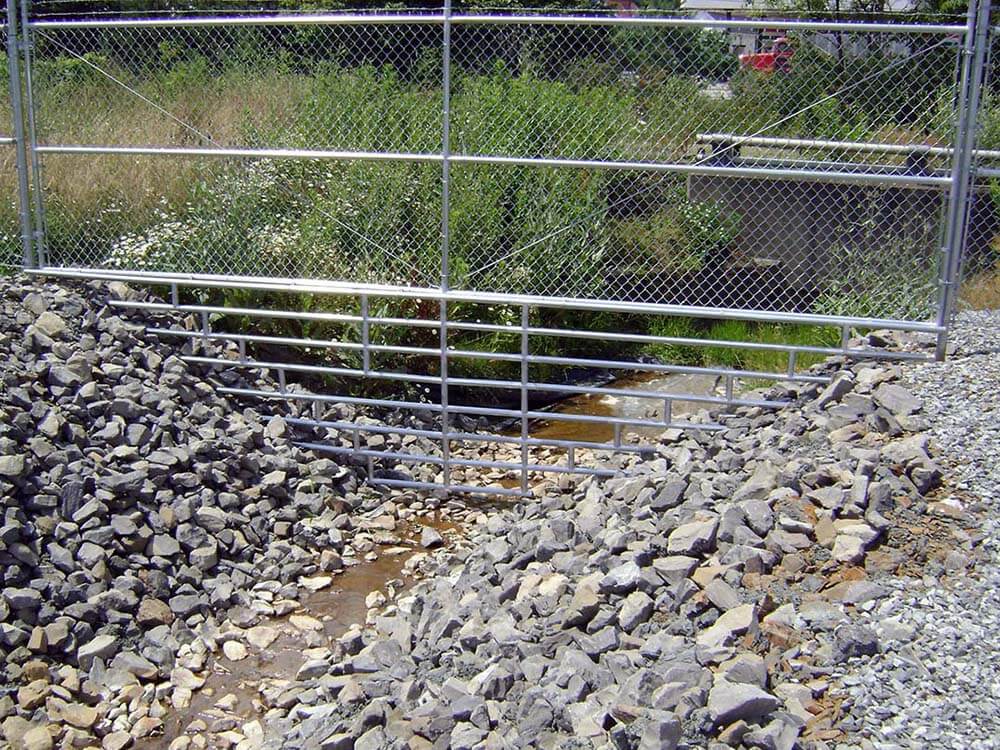 Commercial chain link fence with barbed wire installed over a rocky stream in Western PA