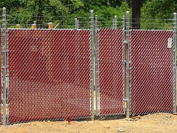 Commercial chain link fence with red privacy slats and barbed wire installed in Western PA