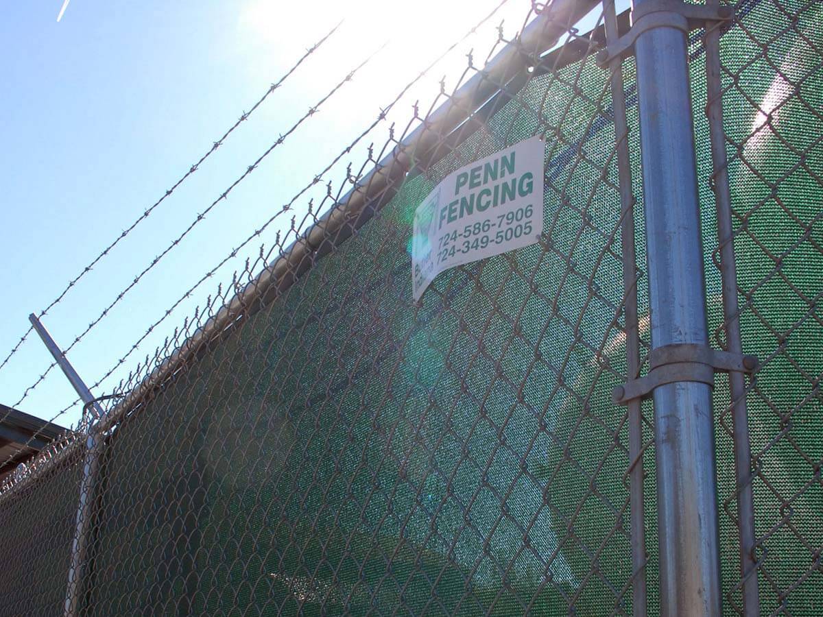 Commercial chain link fence with barbed wire and a green privacy screen installed in Western PA
