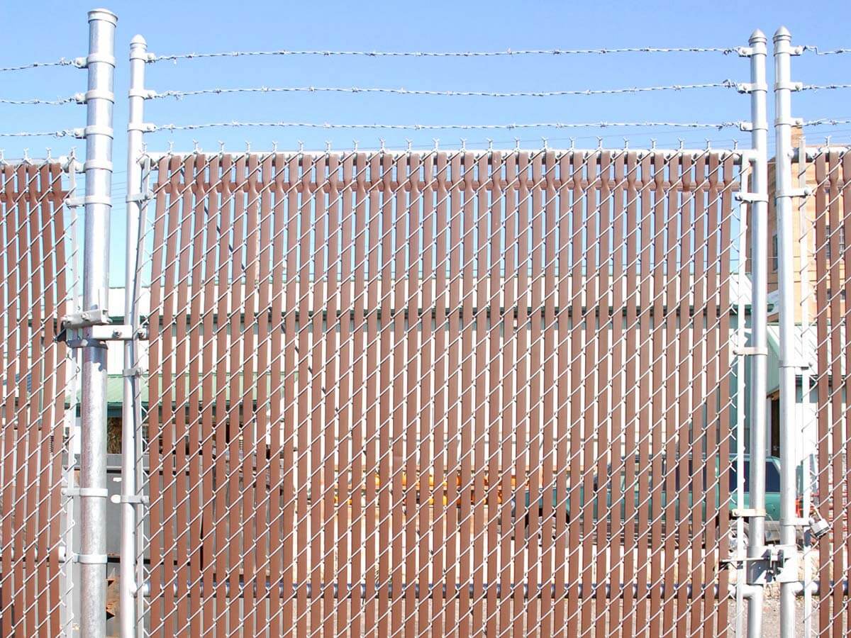 Commercial chain link fence with barbed wire and brown privacy slats installed in Western PA