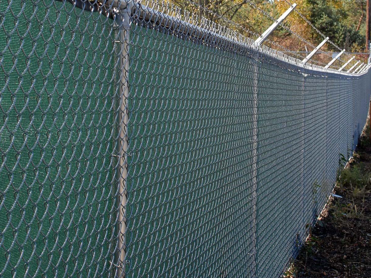 Commercial chain link fence with barbed wire and green privacy screens installed in Western PA