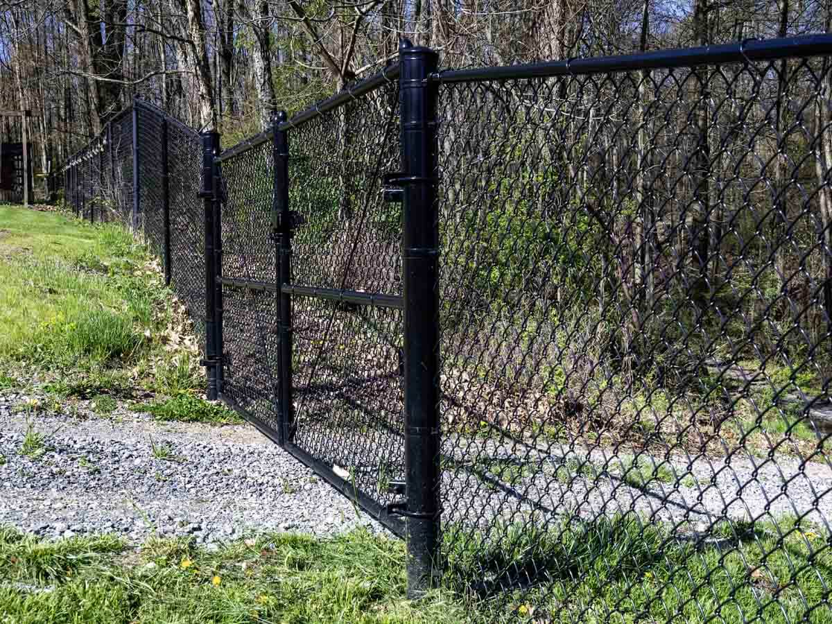 Black chain link fence with gate installed across a gravel driveway in Western Pennsylvania